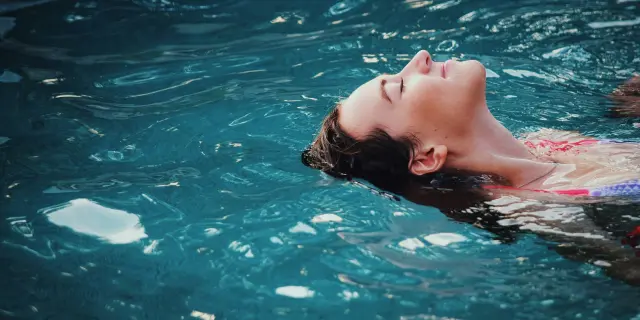 Jeune femme flottant sur le dos dans une piscine