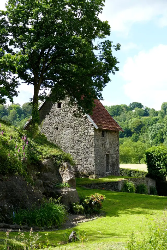 Maison en pierre avec un toit en tuiles rouges entourée d'arbres et de verdure au village Mauny de Hambye