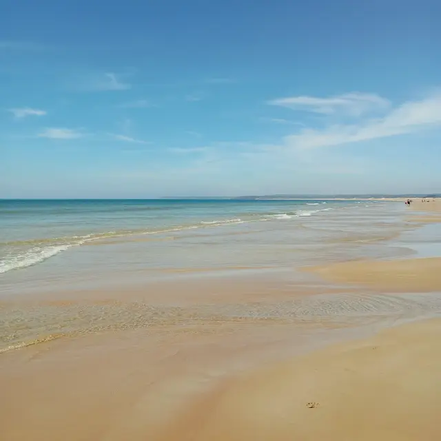 Ansicht eines feinen Sandstrandes mit sanften Wellen und einem blauen Meer unter einem klaren Himmel