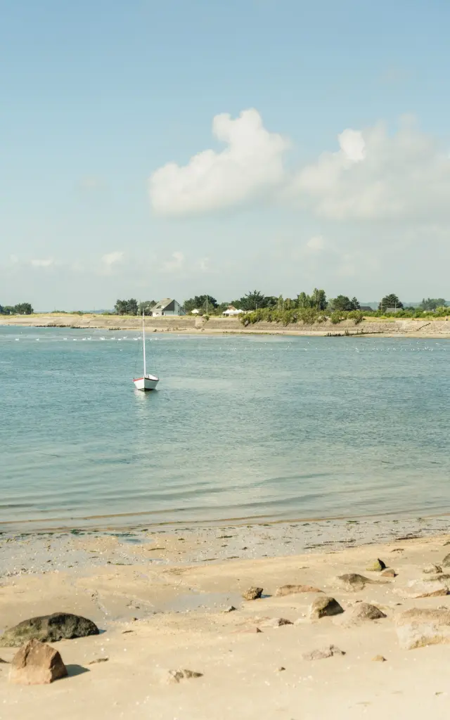 Ein kleines weißes Boot auf einem Sandstrand mit Felsen