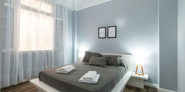 Chambre d'hôtes avec lit double, rideaux blancs et murs gris
