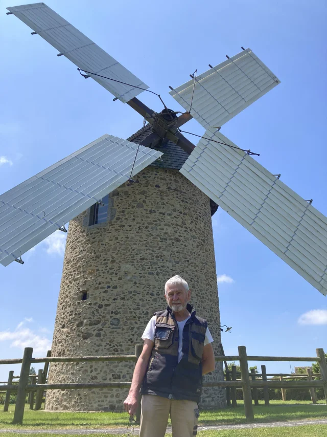 Man standing in front of a stone windmill with modern blades
