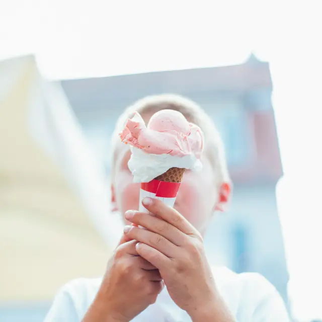 Un enfant tenant une glace à la fraise avec des mains couvertes de glace.