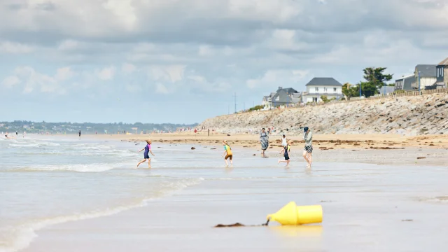 Plusieurs enfants courent sur une plage de sable avec des maisons en arrière-plan à Hauteville-sur-Mer