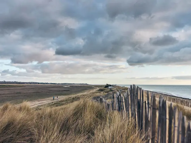 Une plage à Blainville-sur-Mer avec une clôture en bois et des nuages sombres