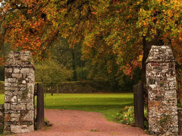 Une entrée en pierre avec un chemin de terre rouge menant au parc de l'abbaye de Hambye