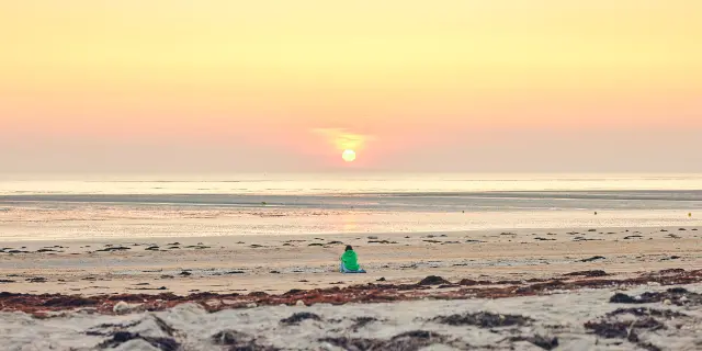 Une personne en silhouette sur une plage de Lingreville au coucher du soleil