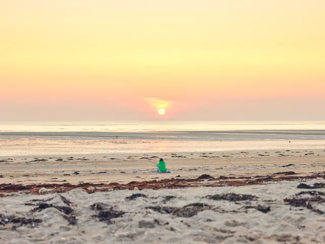 Une personne en silhouette sur une plage de Lingreville au coucher du soleil