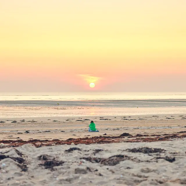 Une personne en silhouette sur une plage de Lingreville au coucher du soleil