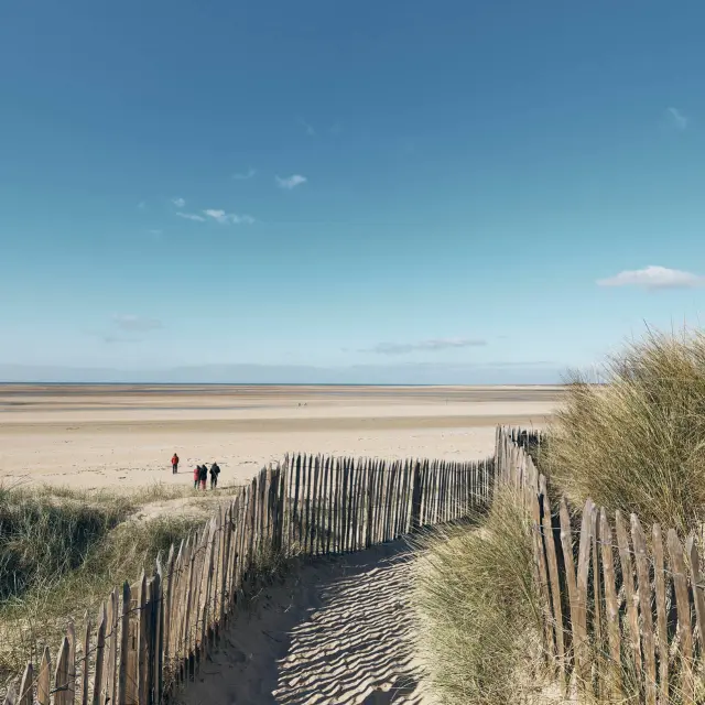 Sentier en bois menant à une plage déserte sous un ciel bleu : Montmartin sur Mer