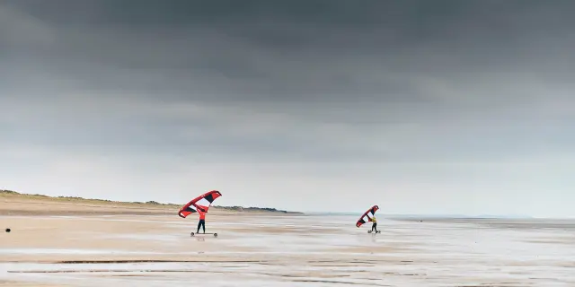 Deux personnes faisant du kitesurf sur une plage déserte sous un ciel nuageux : Hauteville sur Mer