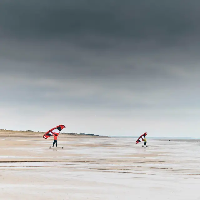 Deux personnes faisant du kitesurf sur une plage déserte sous un ciel nuageux : Hauteville sur Mer