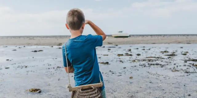 Un enfant observe l'horizon en tenant un seau en plastique sur une plage
