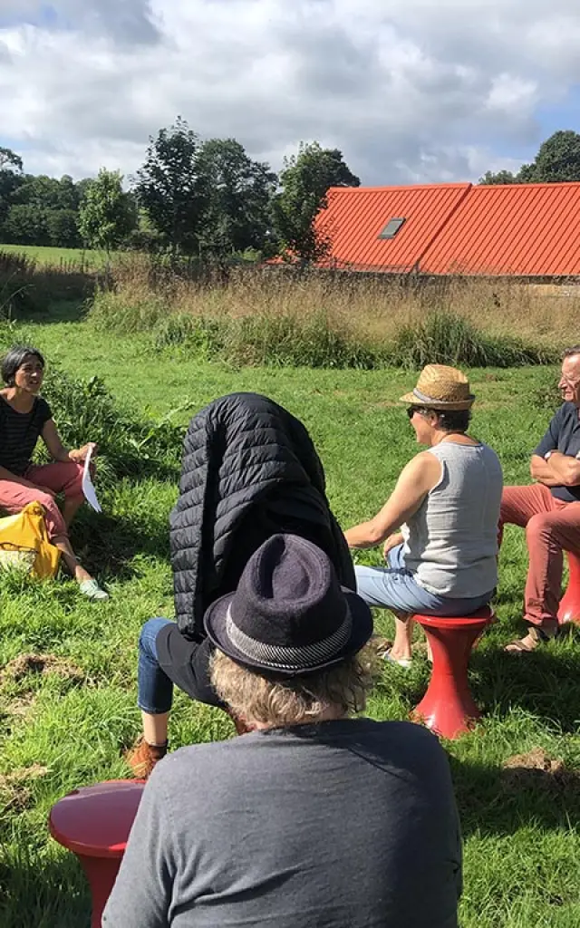Groupe de personnes assises en cercle sur des tabourets rouges dans un champ à Cour avec Vue