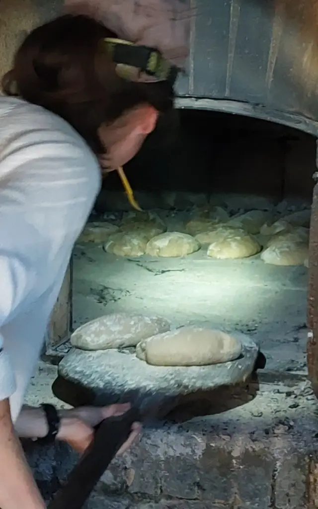 Une personne place des boules de pâte à pain dans un four à bois à la foulerie