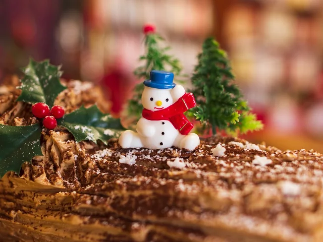 Bûche de Noël décorée avec un bonhomme de neige et des branches de houx