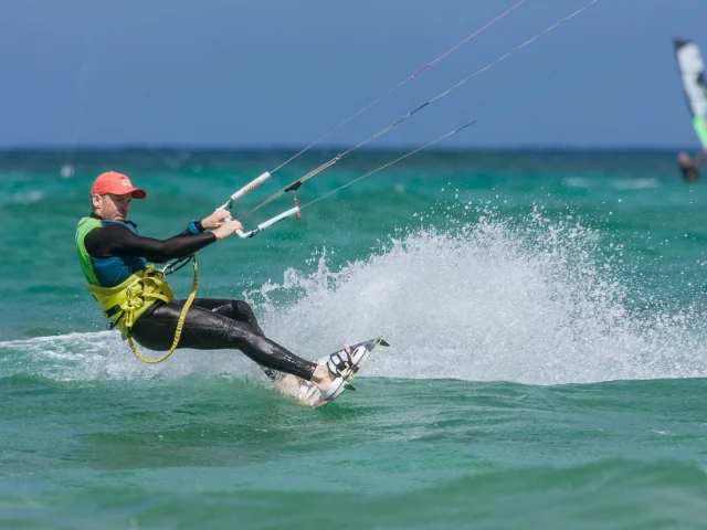 A kitesurfer in a black and yellow wetsuit surfing on turquoise water