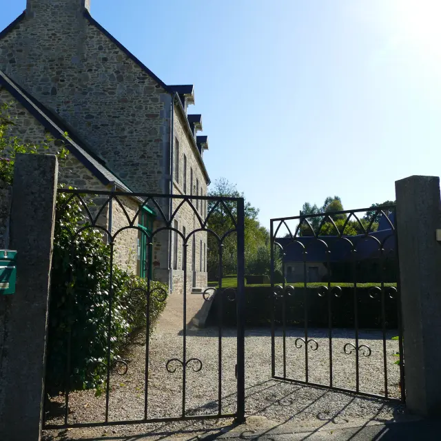 Open wrought iron gate leading to a gravel path in front of a stone house