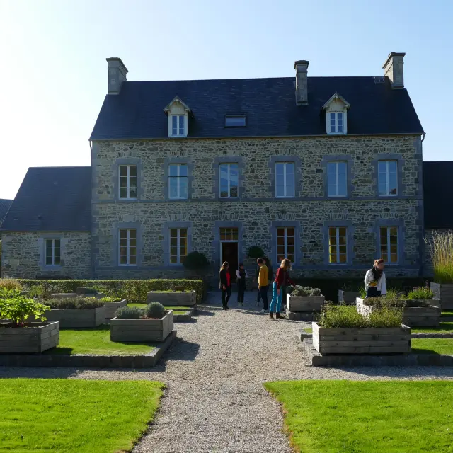 A large stone house with a well-maintained garden and people walking towards the entrance