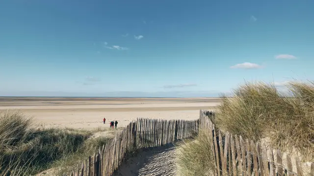 Sentier en ganivelles menant à une plage déserte sous un ciel bleu