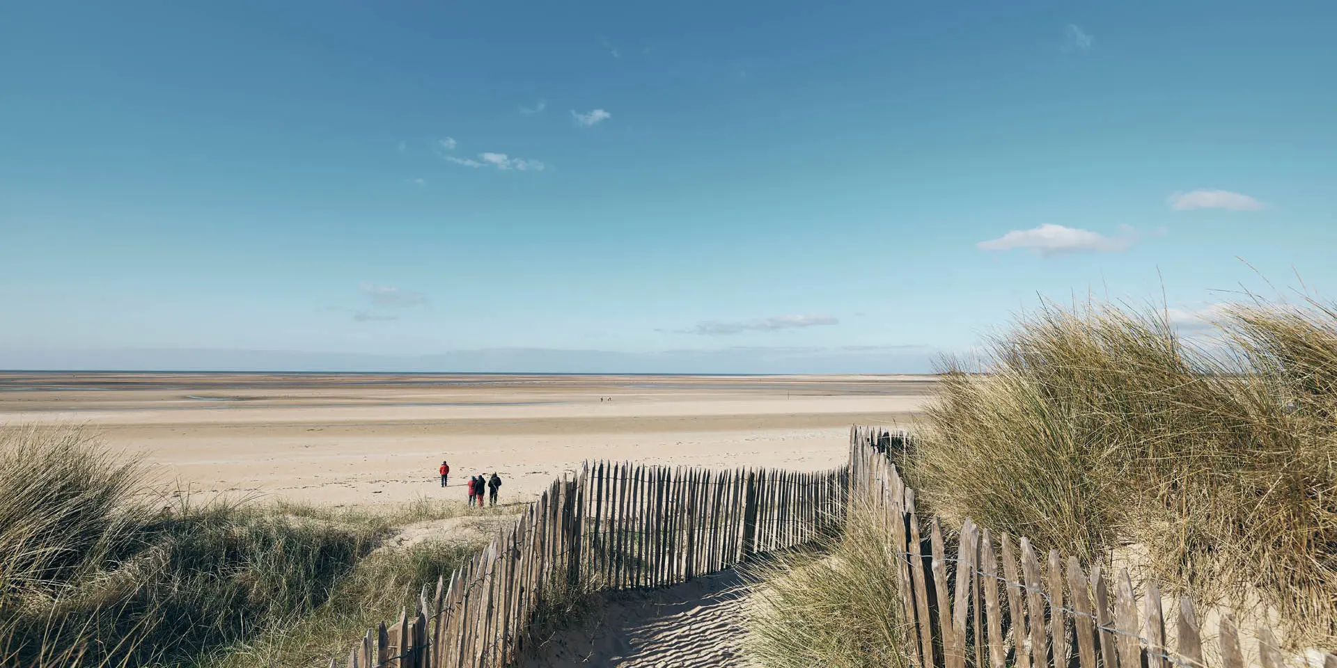 Sentier en ganivelles menant à une plage déserte sous un ciel bleu