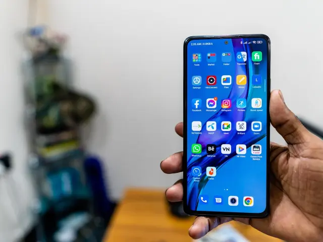 Main tenant un smartphone avec un écran bleu affichant des icônes d'applications