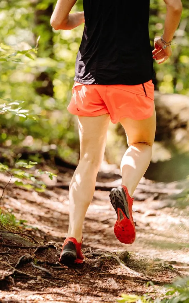 Un coureur en short orange et t-shirt noir court sur un sentier forestier