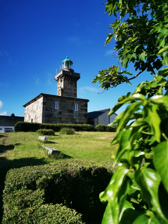 A stone lighthouse with a green lantern on a well-maintained property