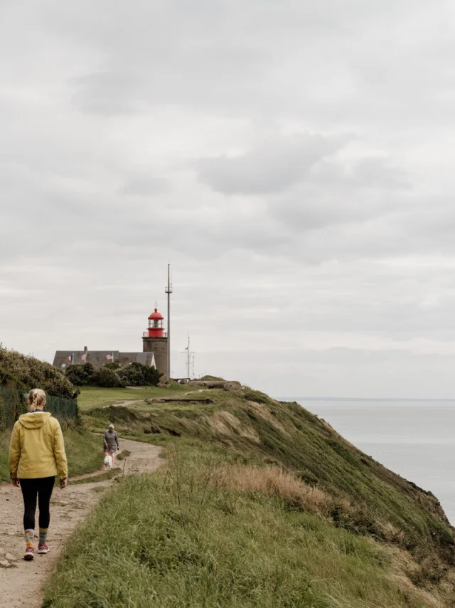 Two people walking towards a lighthouse on a coastal path