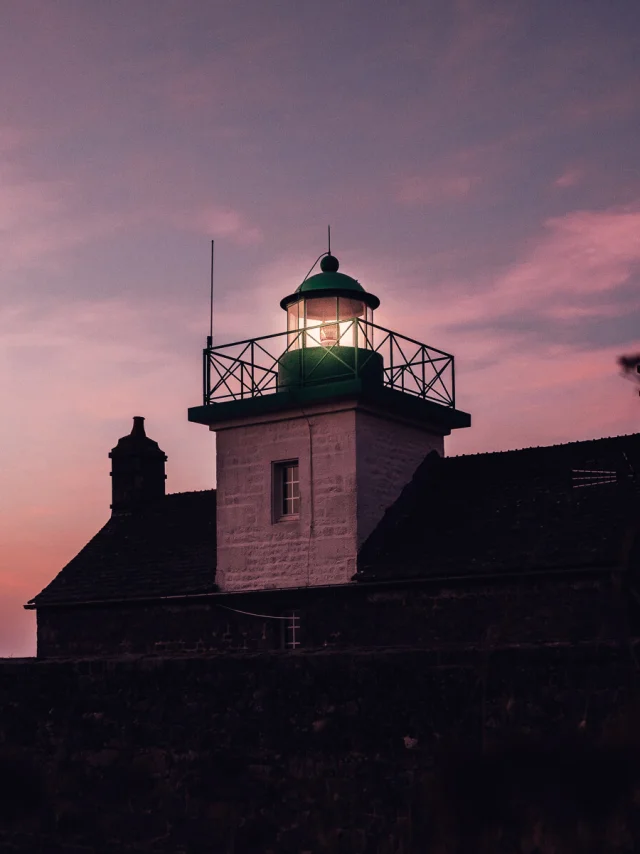 Lighthouse lit at sunset with adjacent buildings