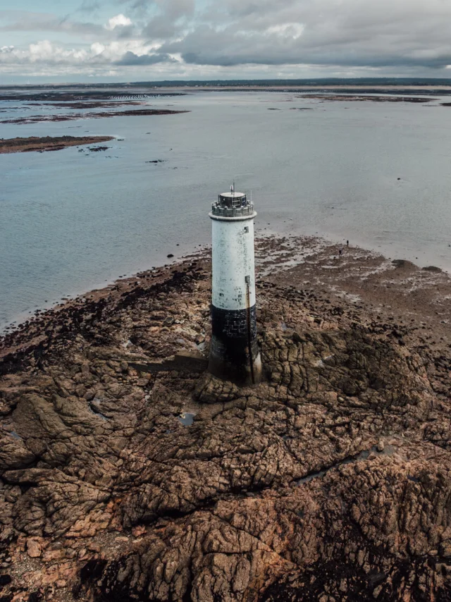 White lighthouse on a rocky outcrop surrounded by water