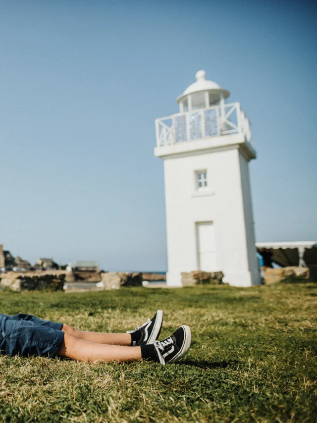 Child lying on the grass near a lighthouse