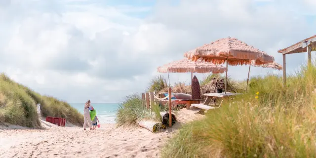 Deux personnes marchant sur une plage avec des parasols et des chaises longues - Paillotte Anneville sur Mer