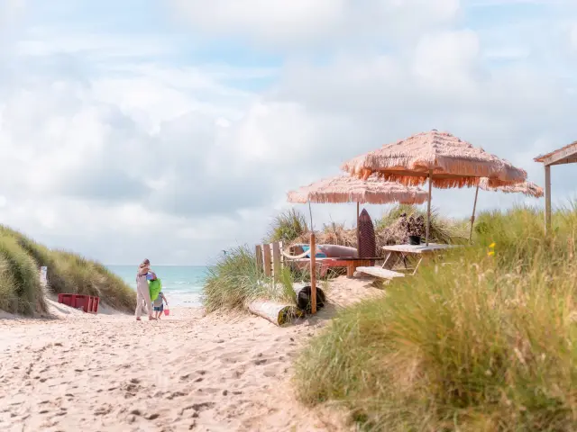 Two people walking on a beach with umbrellas and lounge chairs