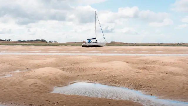 A sailboat stranded on a sandy beach with shallow water