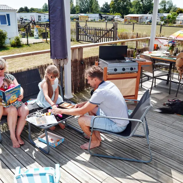 Eine Familie im Campingurlaub, die auf einer Holzterrasse liest und isst