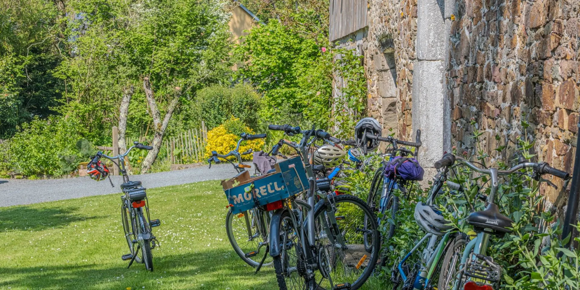 Plusieurs vélos appuyés contre un mur de pierre dans un jardin dans le bocage, campagne