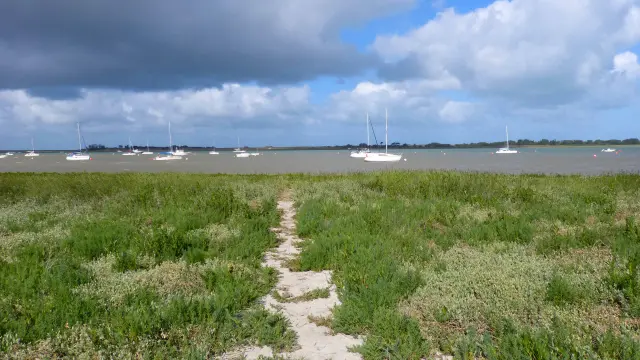 Sandweg, der zu einer Wasserfläche mit Booten in der Ferne führt