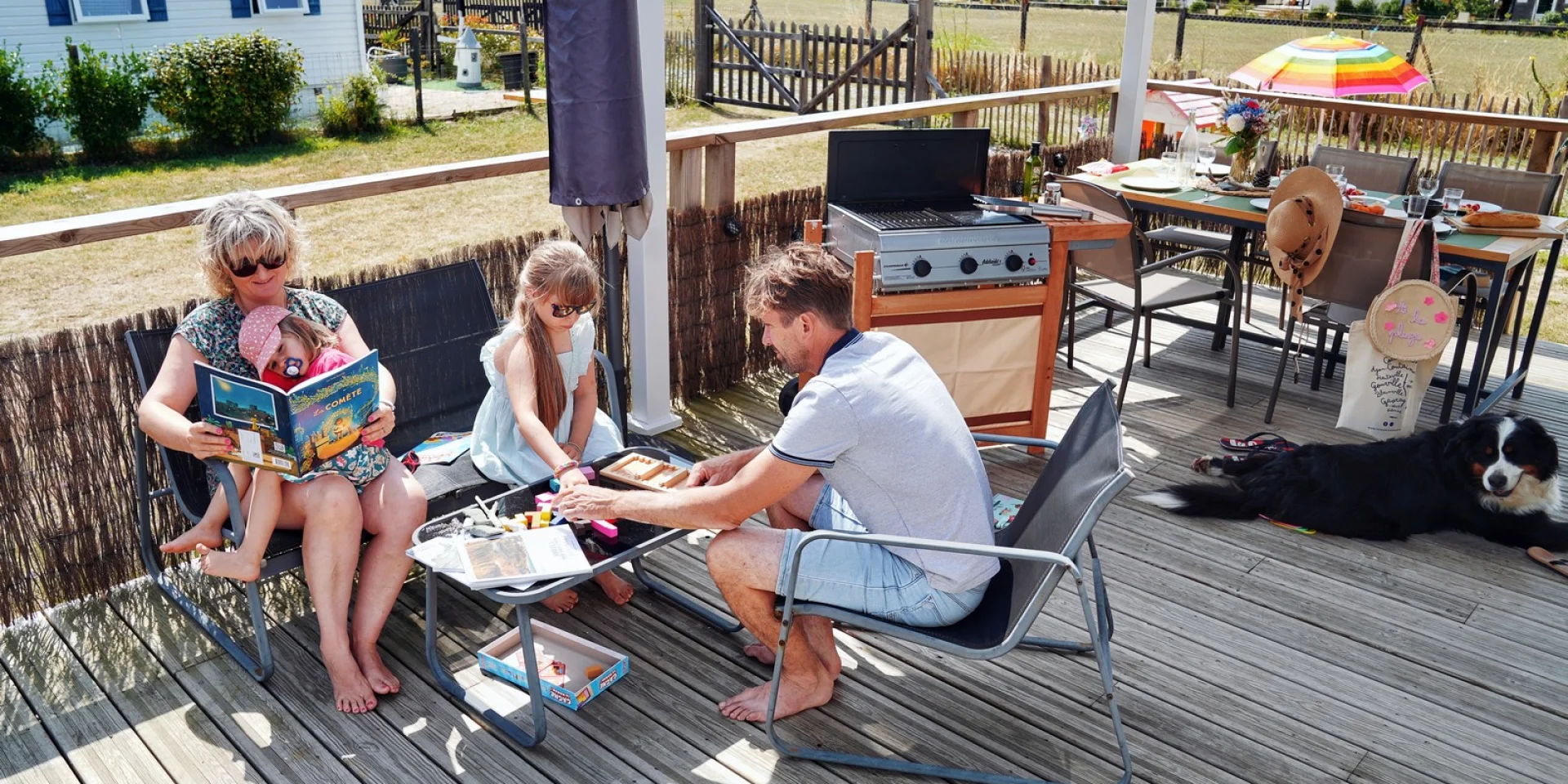 A family on a camping vacation, reading and eating on a wooden terrace