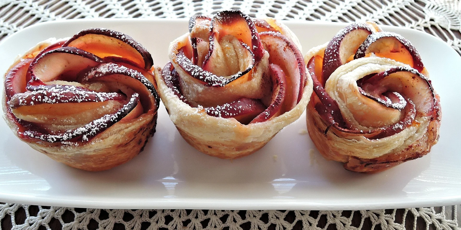 Trois pâtisseries en forme de roses faites avec des pommes et du sucre glace