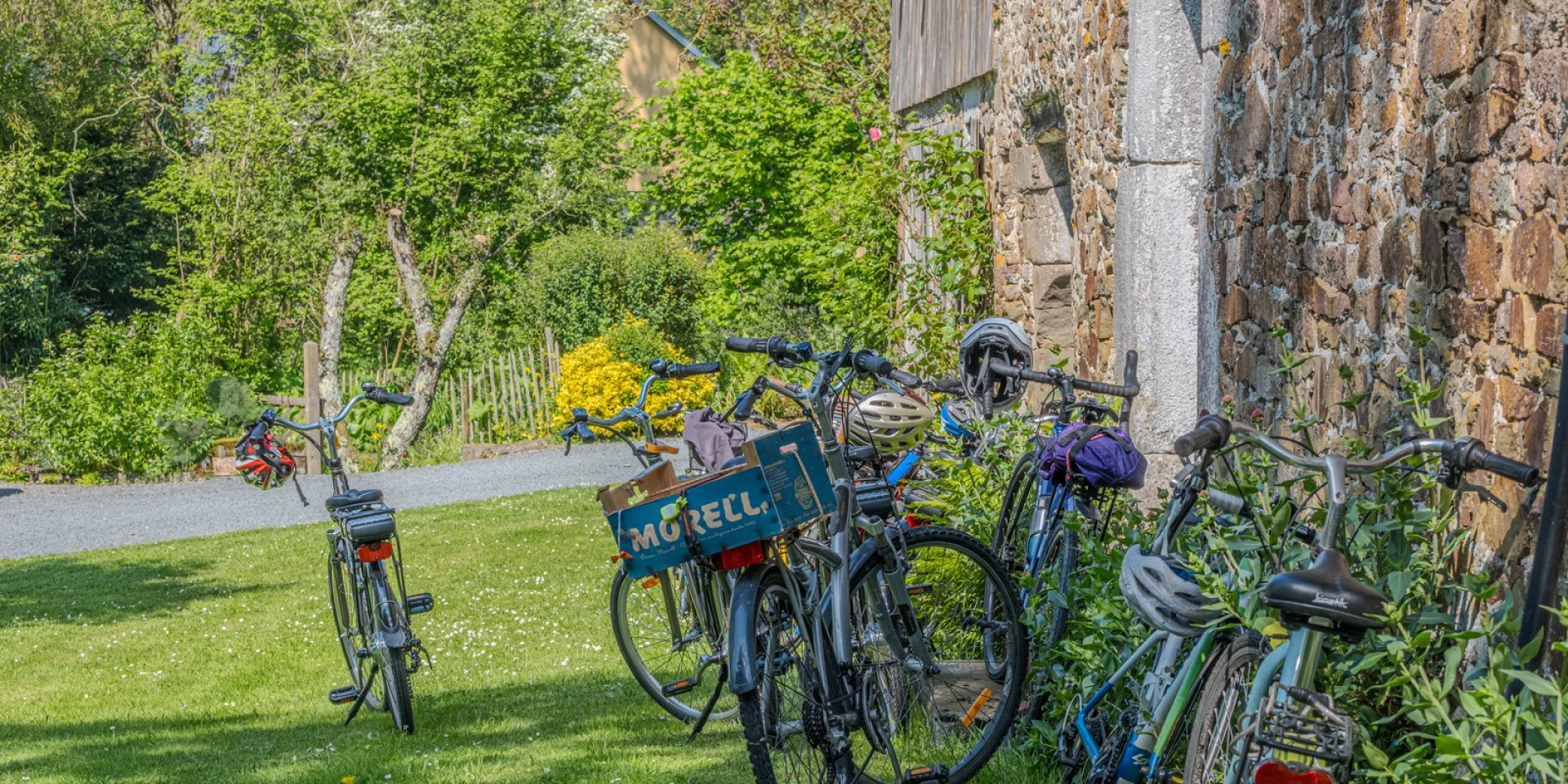 Several bikes leaning against a stone wall in a garden