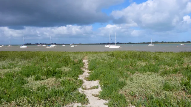 Sandweg, der zu einer Wasserfläche mit Booten in der Ferne führt
