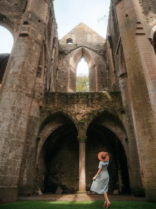 Une femme en robe bleue et chapeau large se tient dans une ruine de l'Abbaye de Hambye