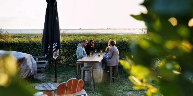 Quatre personnes dînent à une table en plein air près de l'eau : la petite Gare Regnéville sur Mer