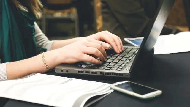 Une personne tape sur un ordinateur portable avec des documents à côté