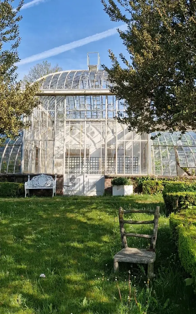 Grande serre en verre avec des bancs en bois devant au château de Cerisy La Salle