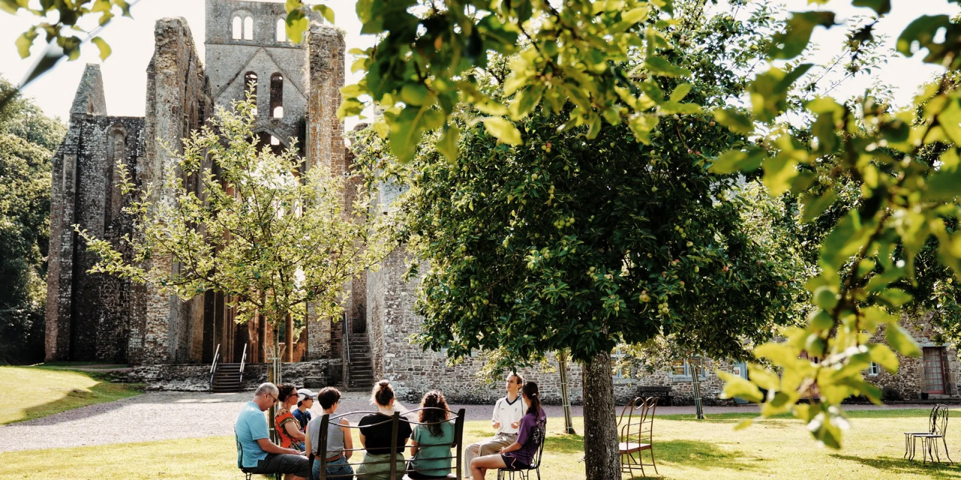 Groupe de personnes assises en cercle devant l'Abbaye de Hambye durant une visite