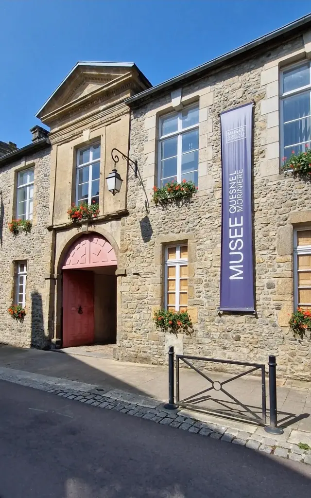 Entrée d'un musée Quesnel Morinière de Coutances avec une porte rouge et des fleurs