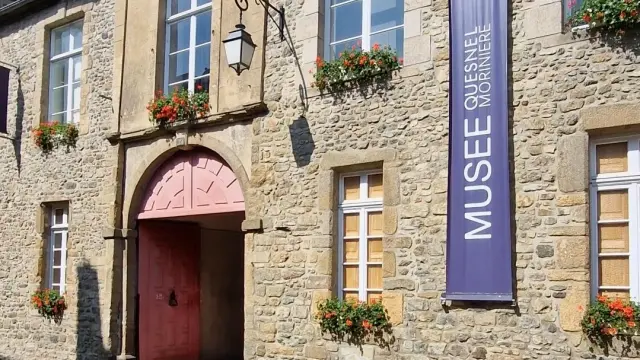 Entrée d'un musée Quesnel Morinière de Coutances avec une porte rouge et des fleurs