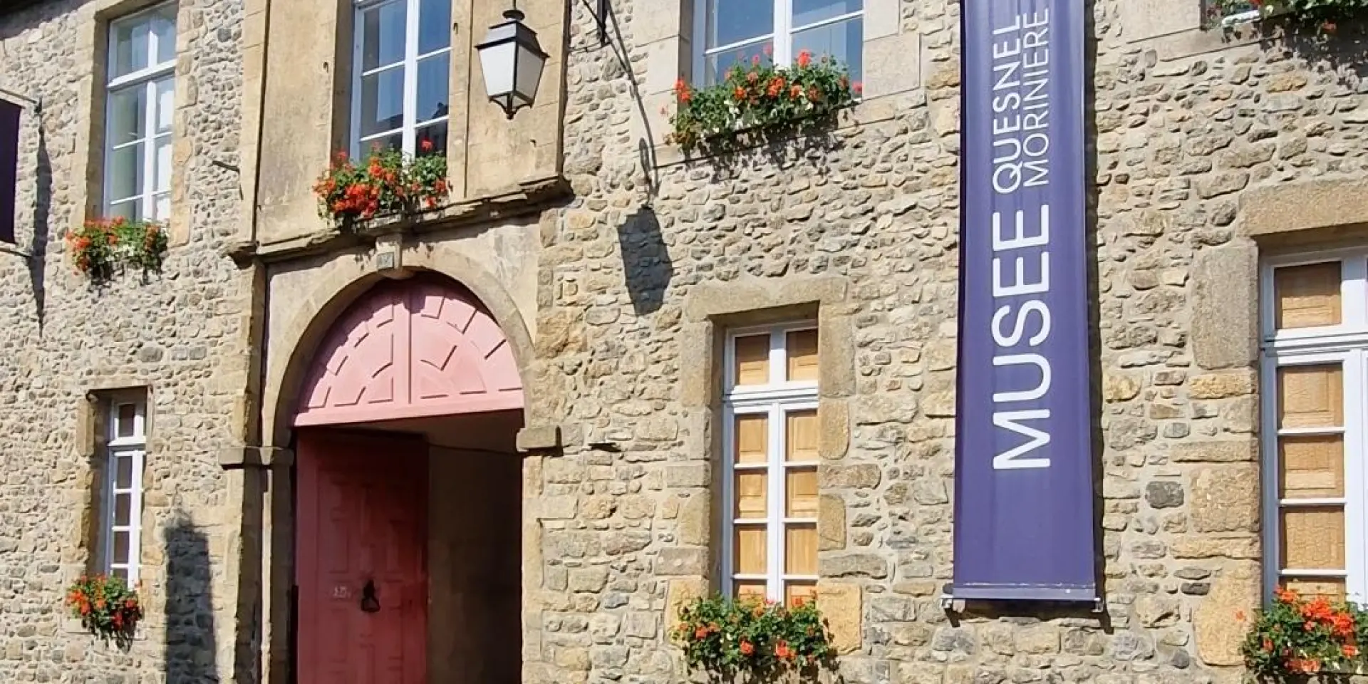 Entrée d'un musée Quesnel Morinière de Coutances avec une porte rouge et des fleurs